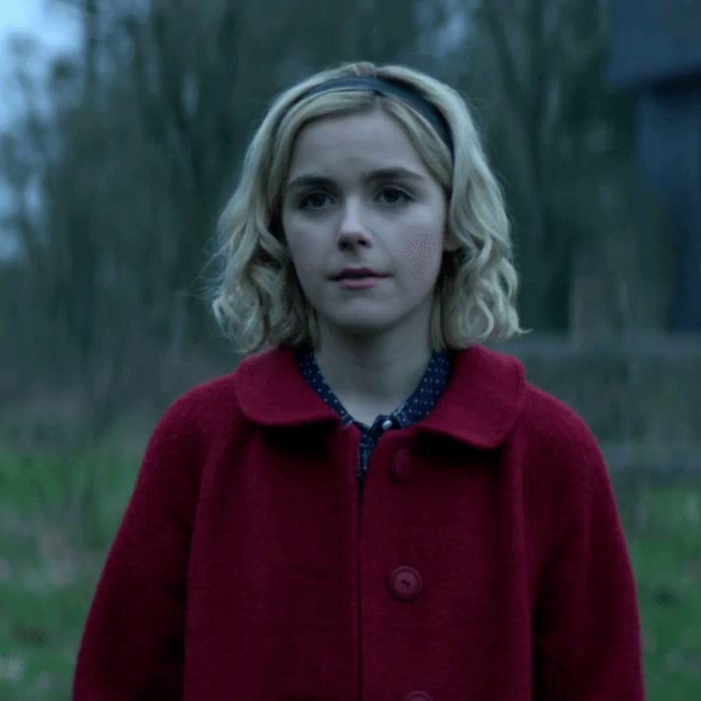 a blonde woman wearing a red coat and a headband smiles for the camera