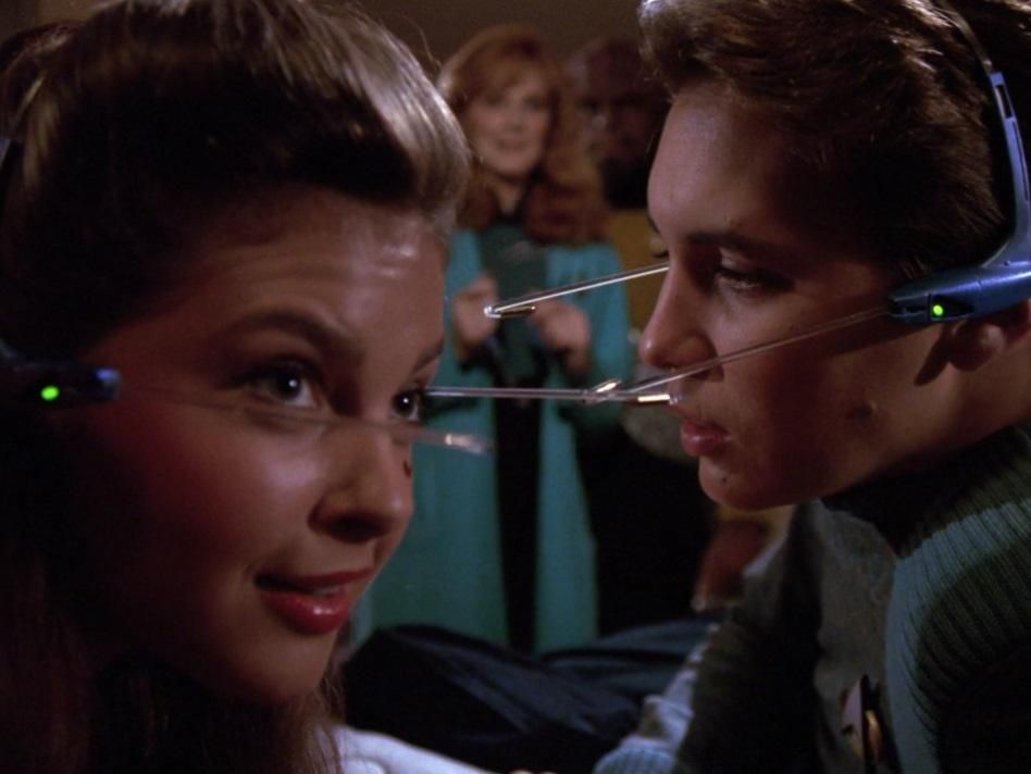 Wesley Crusher and friend wearing fake headsets in ST:TNG “The Game” while his Mum looks on in the background looking thrilled