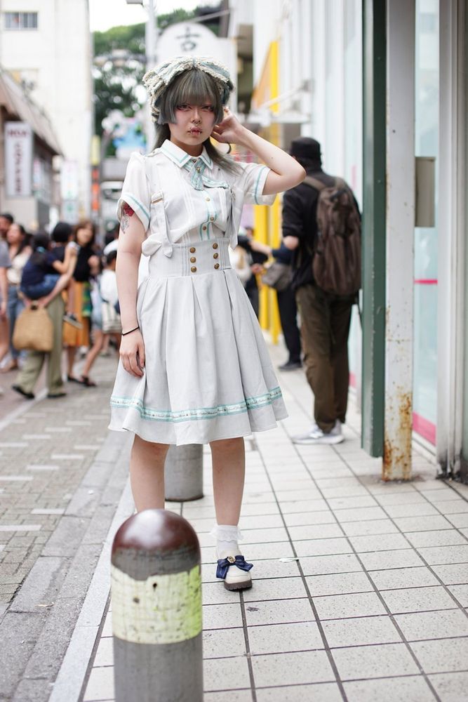 girl with a white outfit and teal accents stands on the sidewalk of a crowded street