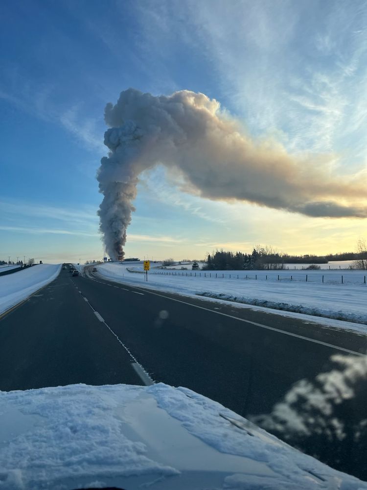 Smoke from a fire next to the highway on a very cold day.