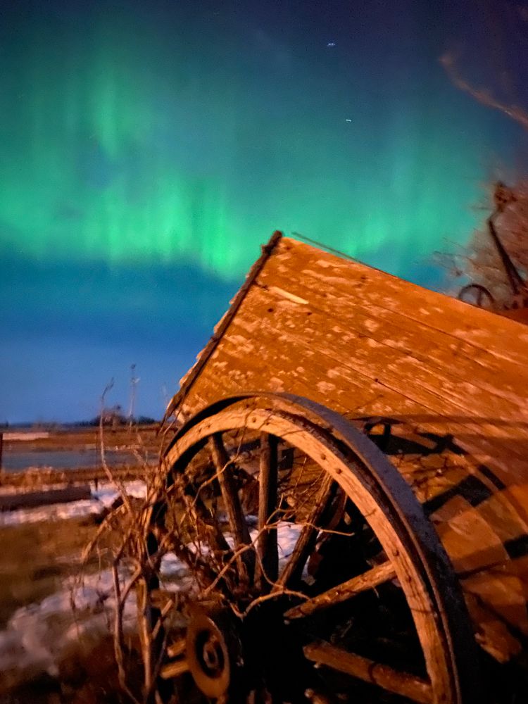Northern lights in the sky with an old cart and wheel in the foreground 
