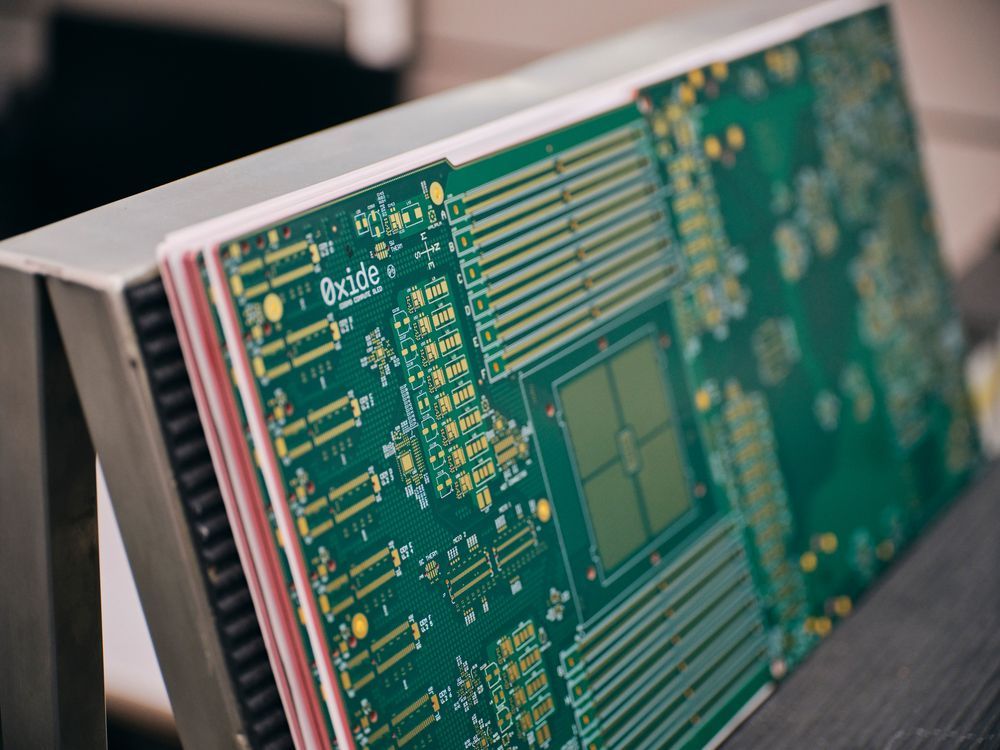 Close-up view of a green Oxide-branded circuit board with gold traces and components during final visual inspection.