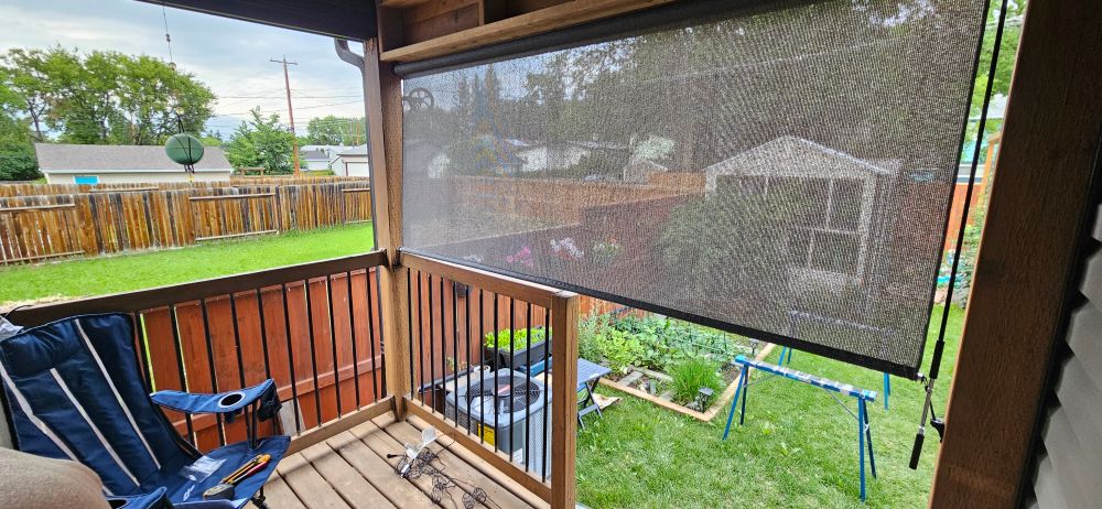A small shaded deck looking out over the garden and greenhouse. A couple of sawhorses can be seen, indicating a work in progress.