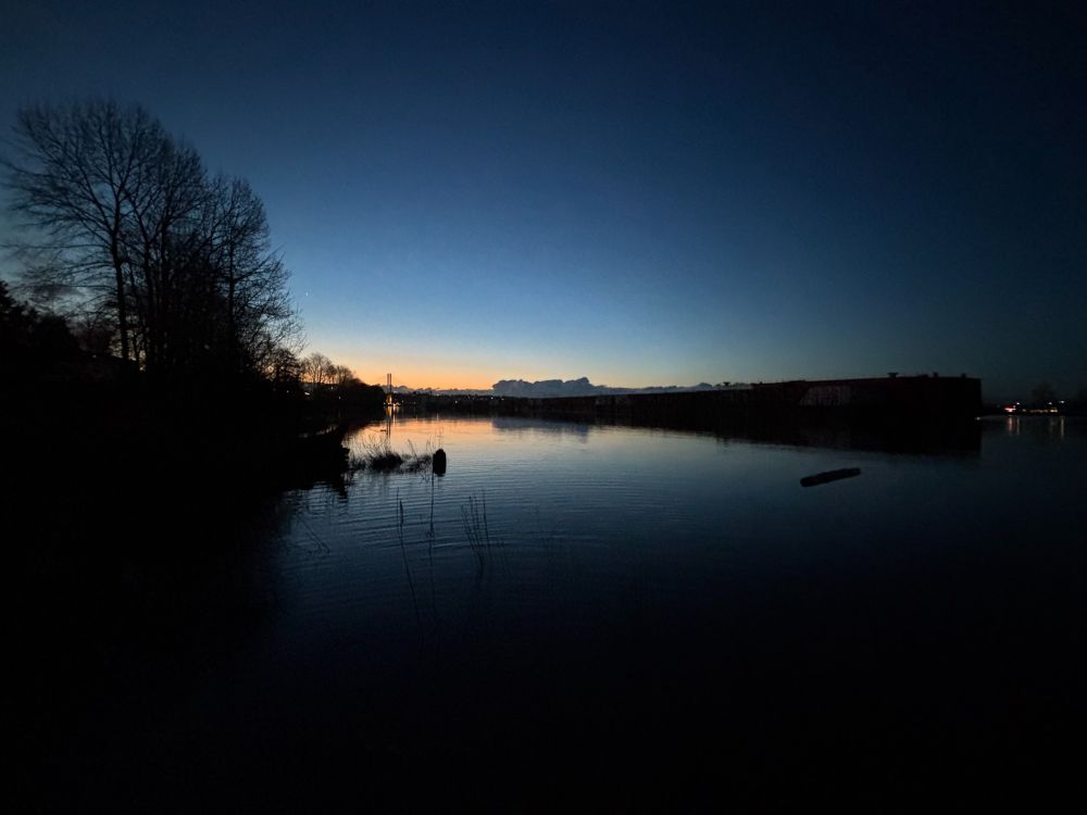 A glowing horizon over the Fraser River. The sky is clear and the river is calm. 