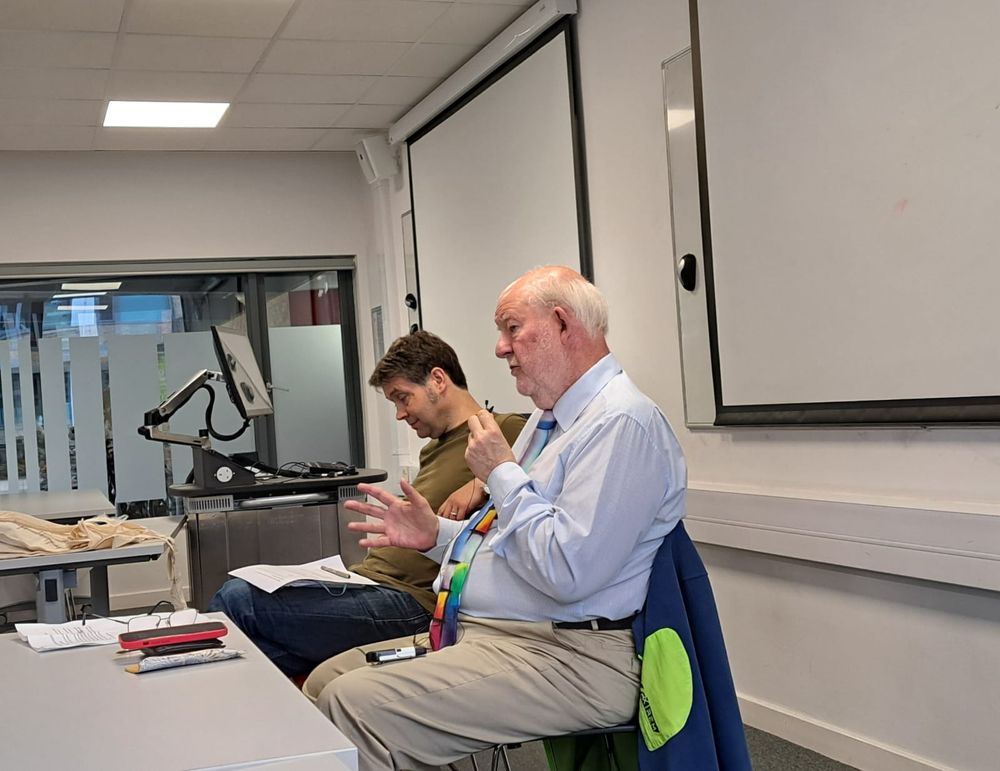 Charles Clarke and Paul Ashwin stitting at a table, talking towards a room of people.