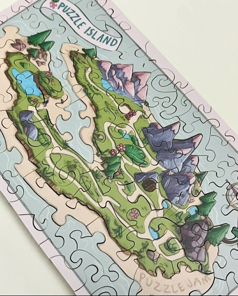 Hand cut wooden jigsaw puzzle of Puzzle Island. The island has puzzle knobs on the shore and in the lake, and the words "Puzzle Jam" written in the sand.
