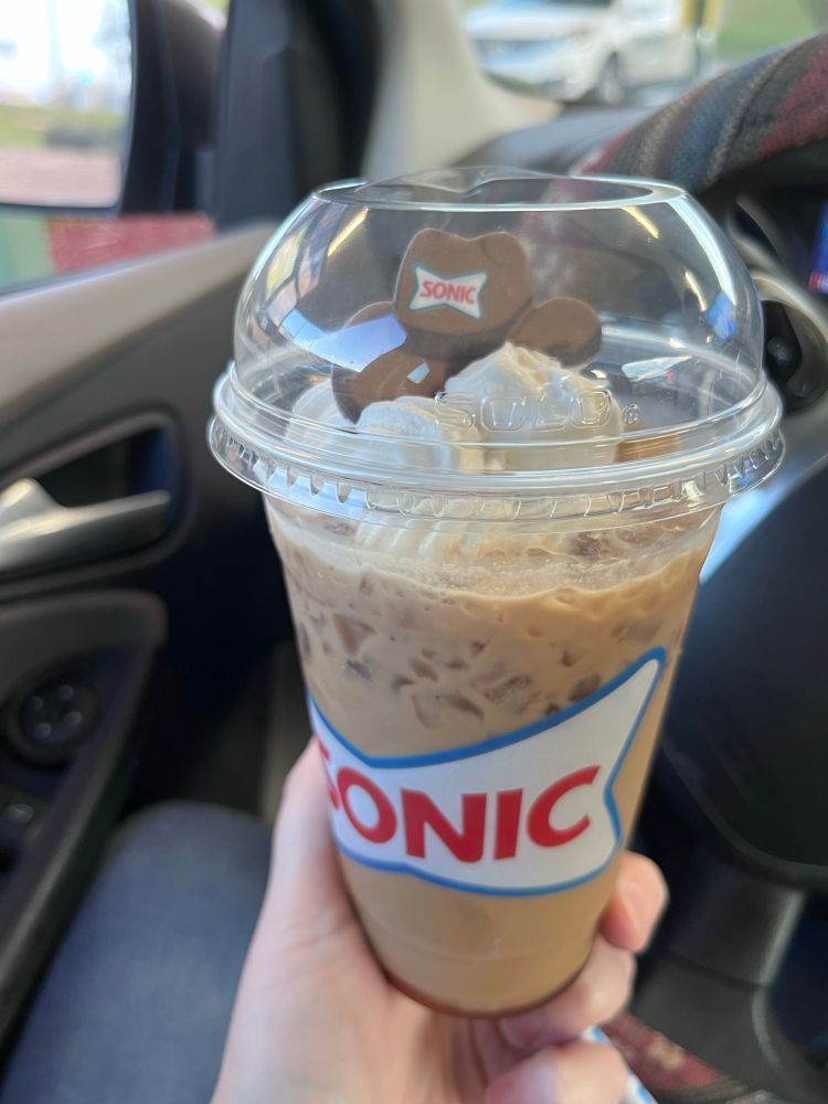 A pale hand holding a bourbon caramel iced coffee from Sonic 