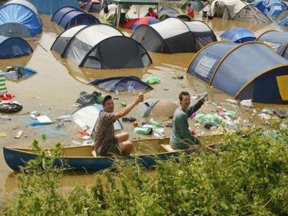 Zu sehen ist ein überschwemmter Campingplatz. Zwei Hoschis fahren in einem
Kanu über den Campingplatz vorbei und prosten in Richtung Kamera.