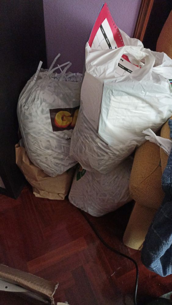 Picture of three plastic and one paper bags full of shredded paper stocked in a corner.