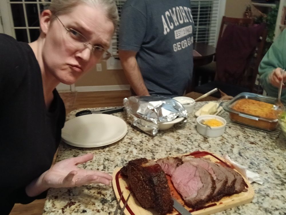 Woman making a silly face as she gestures at a sliced prime rib roast, delicious juices pooling on a cutting board.