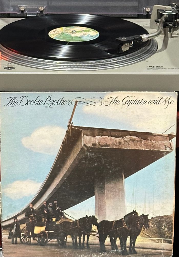 Image of band members on and around a stagecoach hitched to four horses. They are all under an elevated highway bridge. 