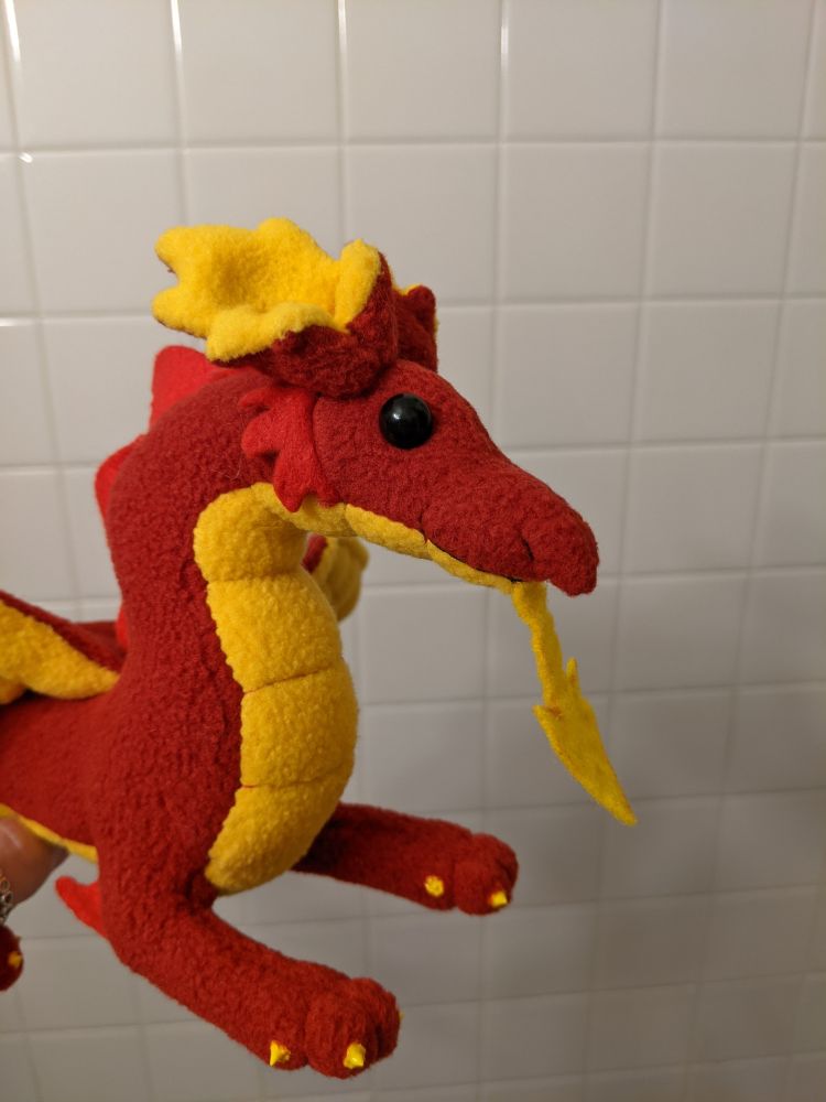 closeup of the red and golden yellow welsh dragon's face and arrow pointed tongue. they have black bead eyes, rough cheeks, a pointy nose/muzzle, and large frilled ears