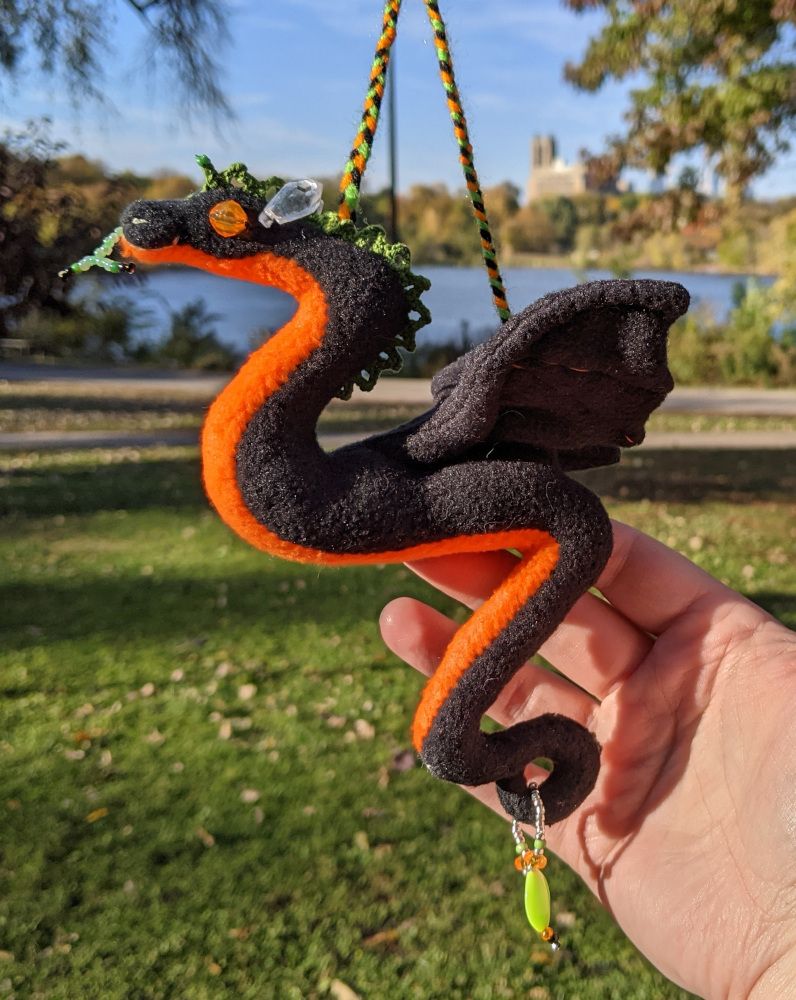 a small black dragon ornament with an orange underbelly and green lace crest
