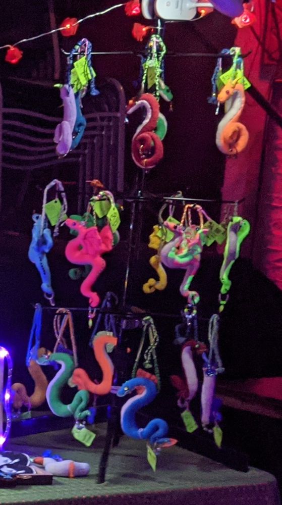 another shot of the dragon plushies that are missing. of the 6 winged dragons in the middle, i hadn't actually gotten any of them listed in my kofi shop yet but there's a lighter blue one, a green one, a yellow one, a neon yellow/greenish one, a neon pink one, and a neon mixed green/pink/orange patterned one