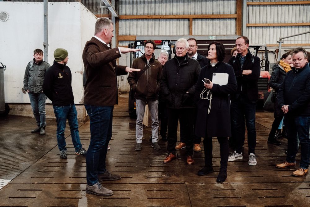 In einer Halle steht eine Gruppe von Menschen. Vor einem Gabelstapler spricht eine Person.