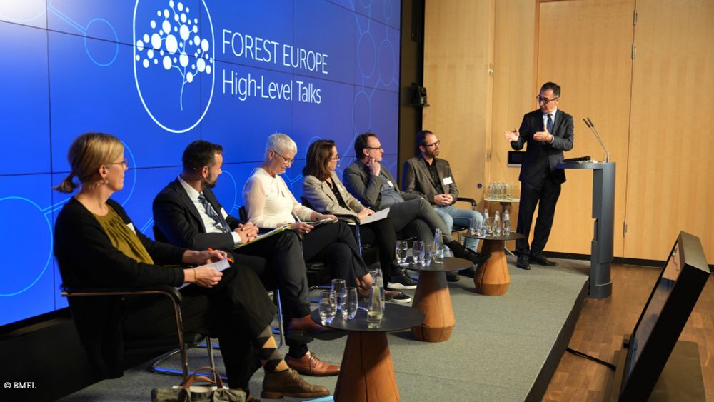 Bundeslandwirtschaftsminister Cem Özdemir hält eine Rede am Pult. Neben ihm sitzen 3 Frauen und 3 Männer auf einem Podium. Auf der Leinwand steht: "Forest Europe - High-Level Talks".