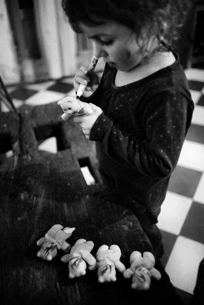 Une petite fille dessine des cheveux sur des petits oursons en peluche.