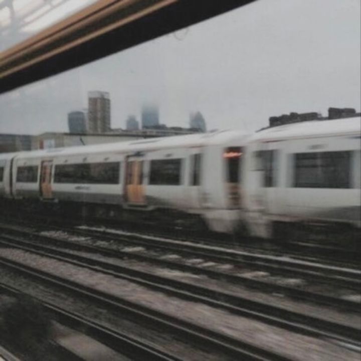 A moving train glides through a bustling cityscape under a blanket of gray clouds