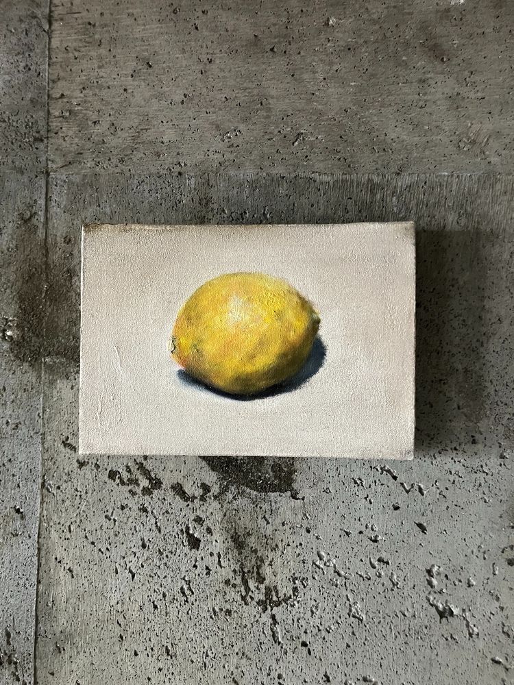 白い背景にレモンがひとつ描かれた油彩画がコンクリートの壁にかけられている。