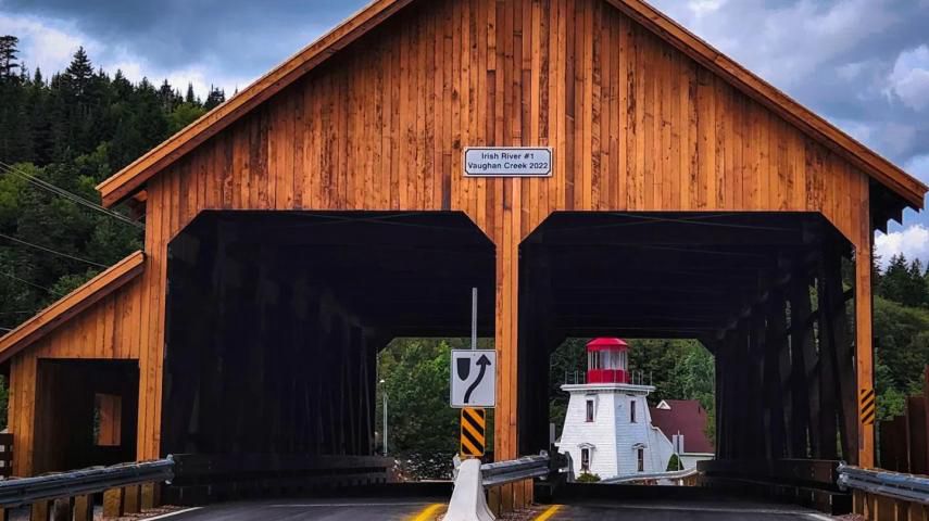 A two lane wooden covered bridge near a lighthouse 