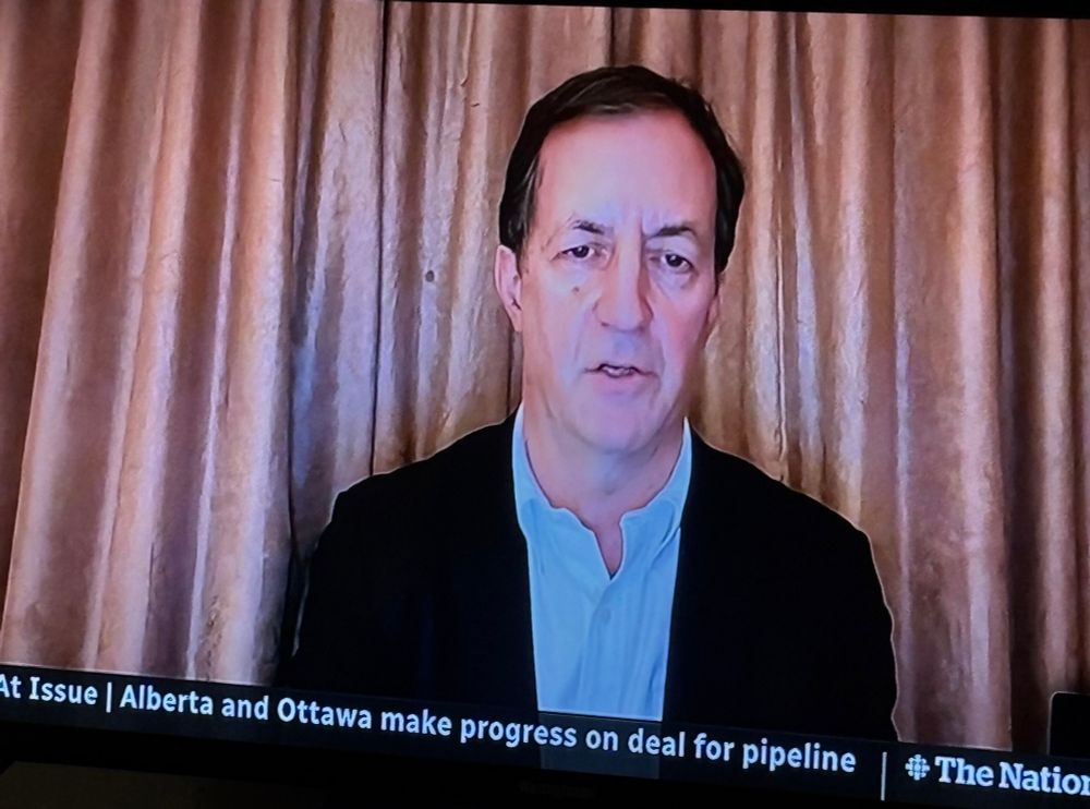 A tired man on a TV screen in front of a golden beige curtain 
