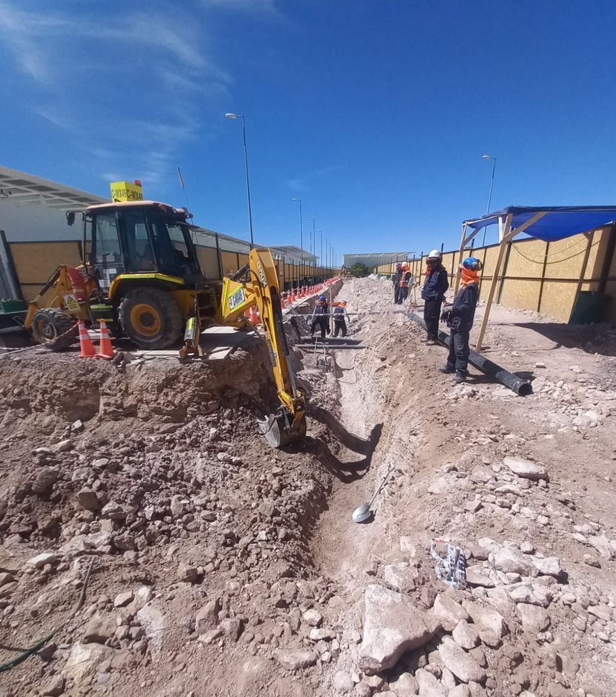 A construction site at ALMA Observatory with a crane digging and workers in hardhats watching. The ground is being broken in preparation for the construction of the new OSF Correlator Room.