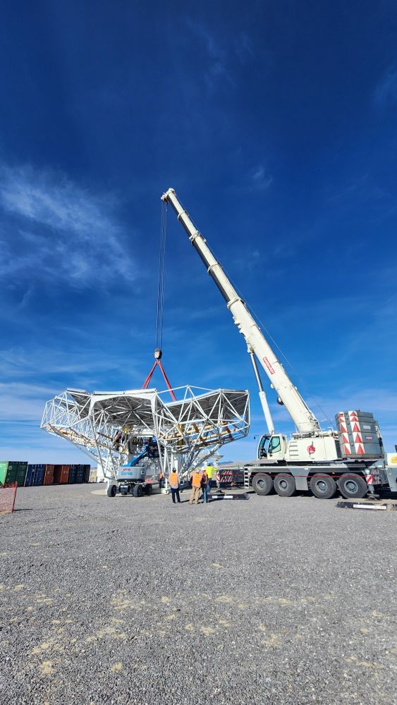 A large crane getting ready to lift a big, geometric metal structure - the ngVLA prototype antenna dish. The sky behind the crane and dish is brilliant blue with faint wispy clouds.
