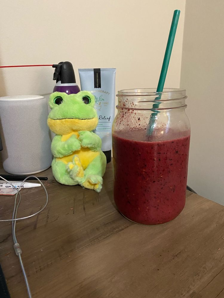 a berry smoothie in a large glass with a frog plush next to it