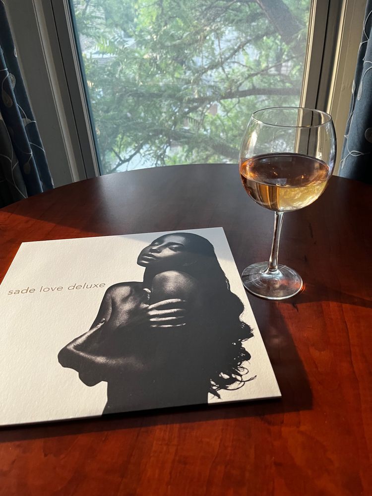 Sade Love Deluxe vinyl album laying on coffee table next to glass of rosé wine. 