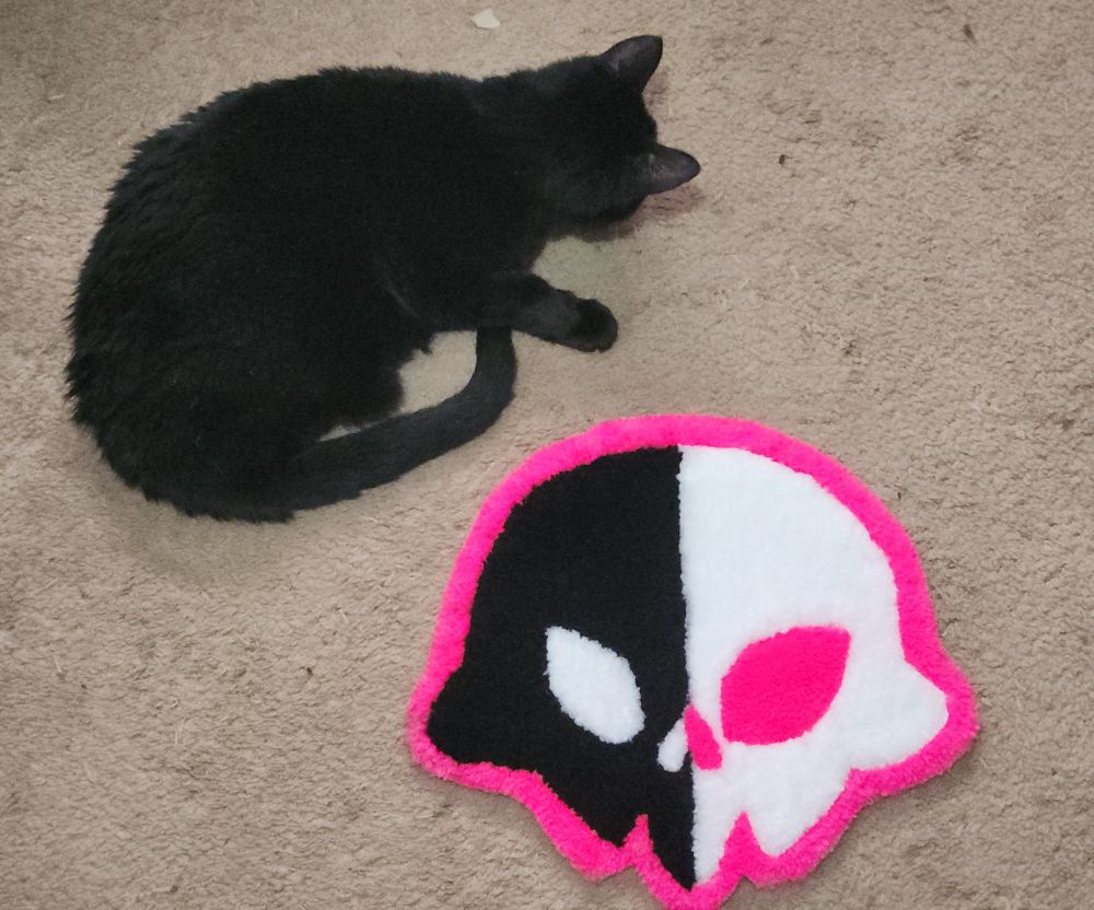 Rug shaped like a cartoon skull next to a black cat.