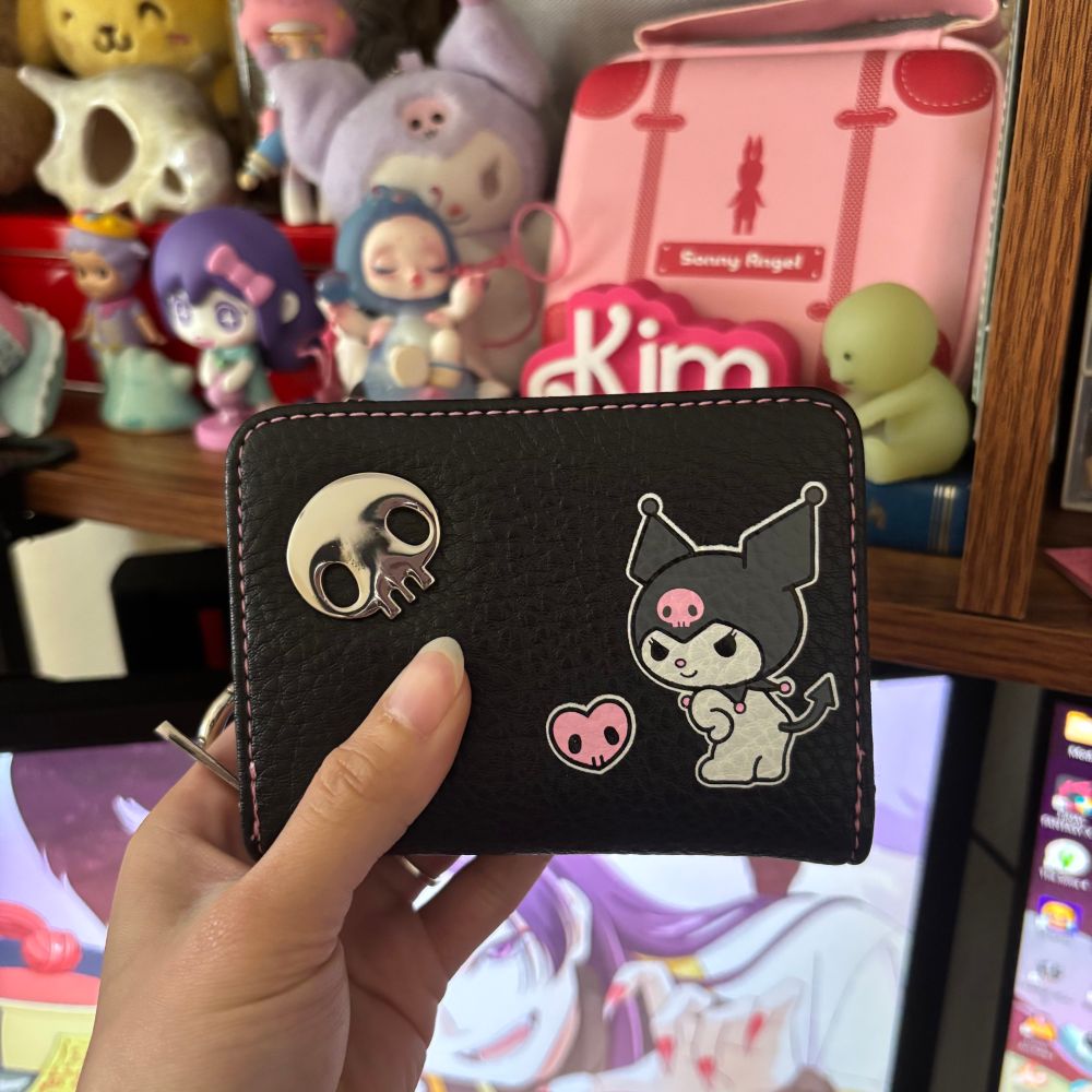 Black leather kuromi wallet with pink stitching :3   There is a metal skull on the top left corner and on the right side of the wallet is an image of kuromi looking back with her hands on her hips. 