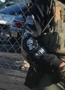 Picture of arm with skull insignia patch, black and white U.S. flag.