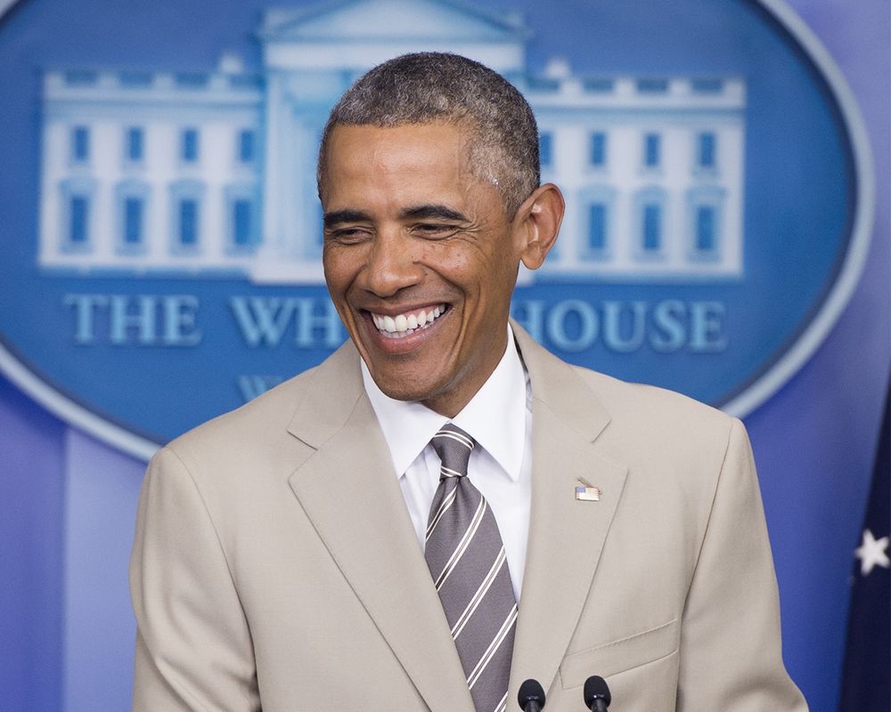 Barack Obama smiling  in the White House press room. Wearing his iconic tan suit. 