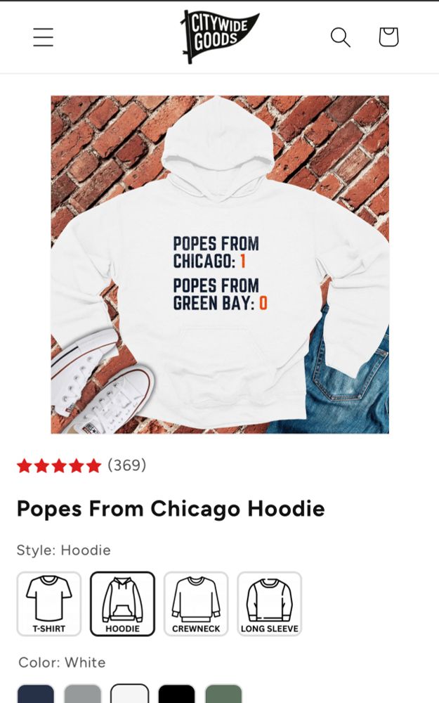 A white hoodie is laid flat on a brick-patterned background alongside white Converse-style sneakers and a pair of folded blue jeans. The hoodie has bold navy and orange text on the front that reads: “POPES FROM CHICAGO: 1” and underneath it “POPES FROM GREEN BAY: 0.” The product listing shows a 5-star rating with 369 reviews and the title “Popes From Chicago Hoodie,” with style options displayed below.