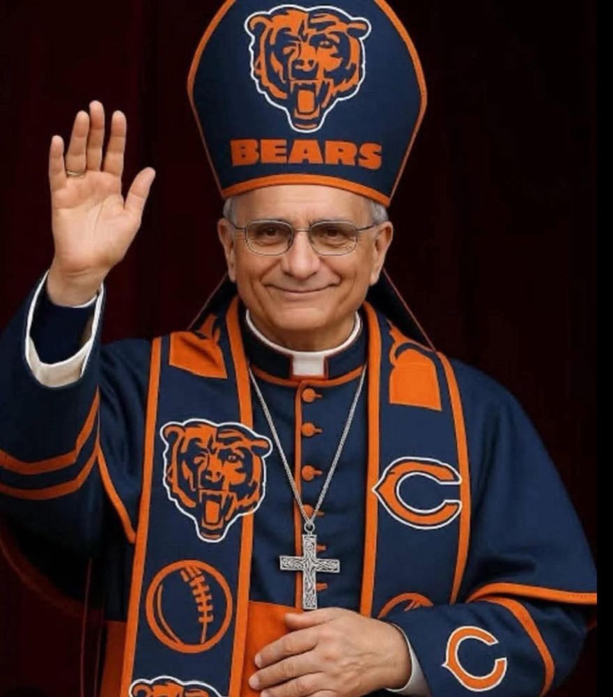 A man dressed in full papal-style robes customized with Chicago Bears colors and logos. His tall mitre hat is navy blue with an orange Bears bear-head logo and the word “BEARS” across the front. His robe and stole also feature multiple Bears logos, a football icon, and orange trim. He smiles gently and raises one hand in a blessing gesture.
