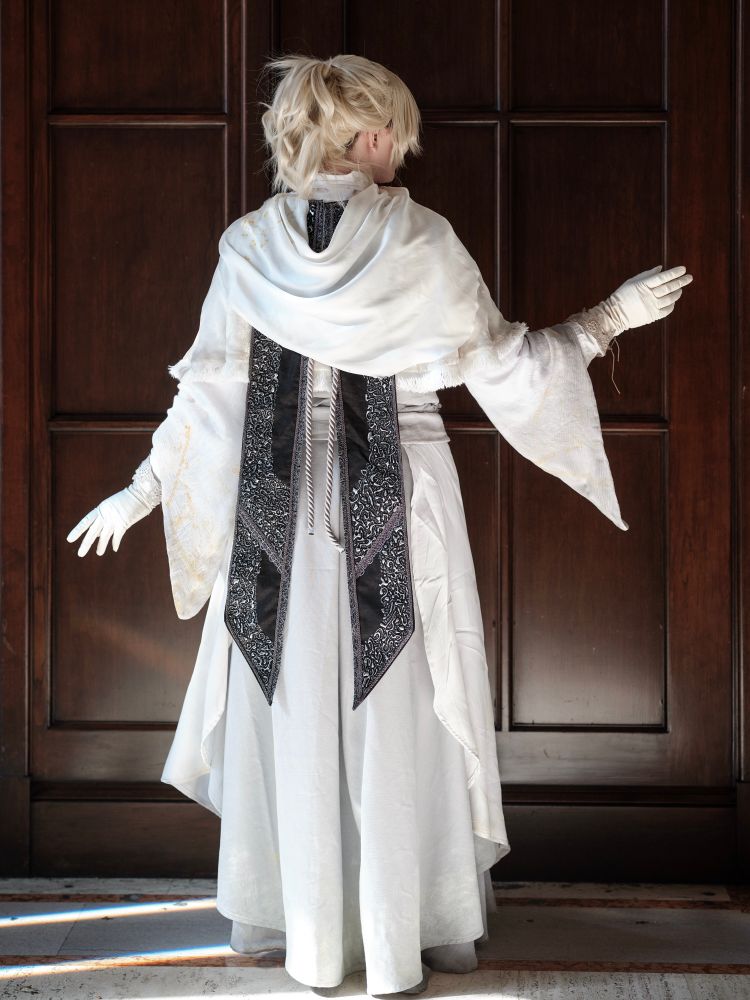 Ridley cosplaying Iosefka from Bloodborne. This pic showcases the back of the cosplay, which is all white except for the black and silver embroidered  panels at the center back 