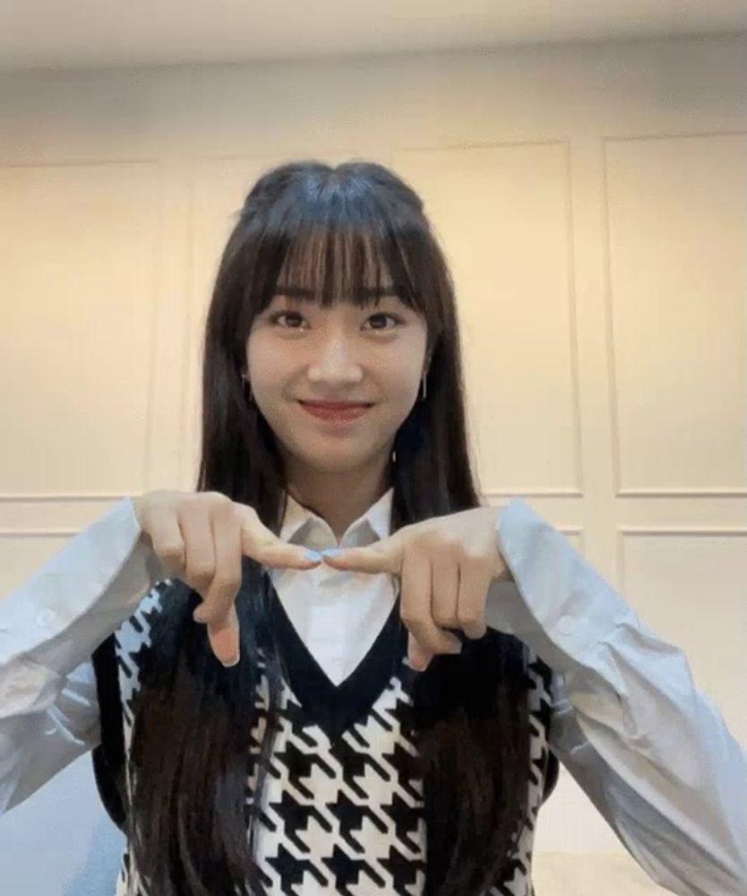 a girl wearing a black and white vest making a heart with her fingers