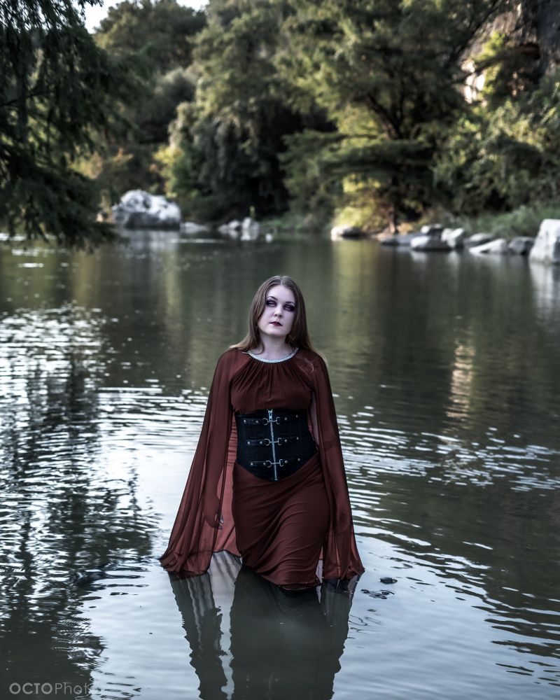 A woman stands in water, surrounded by trees and rocks
