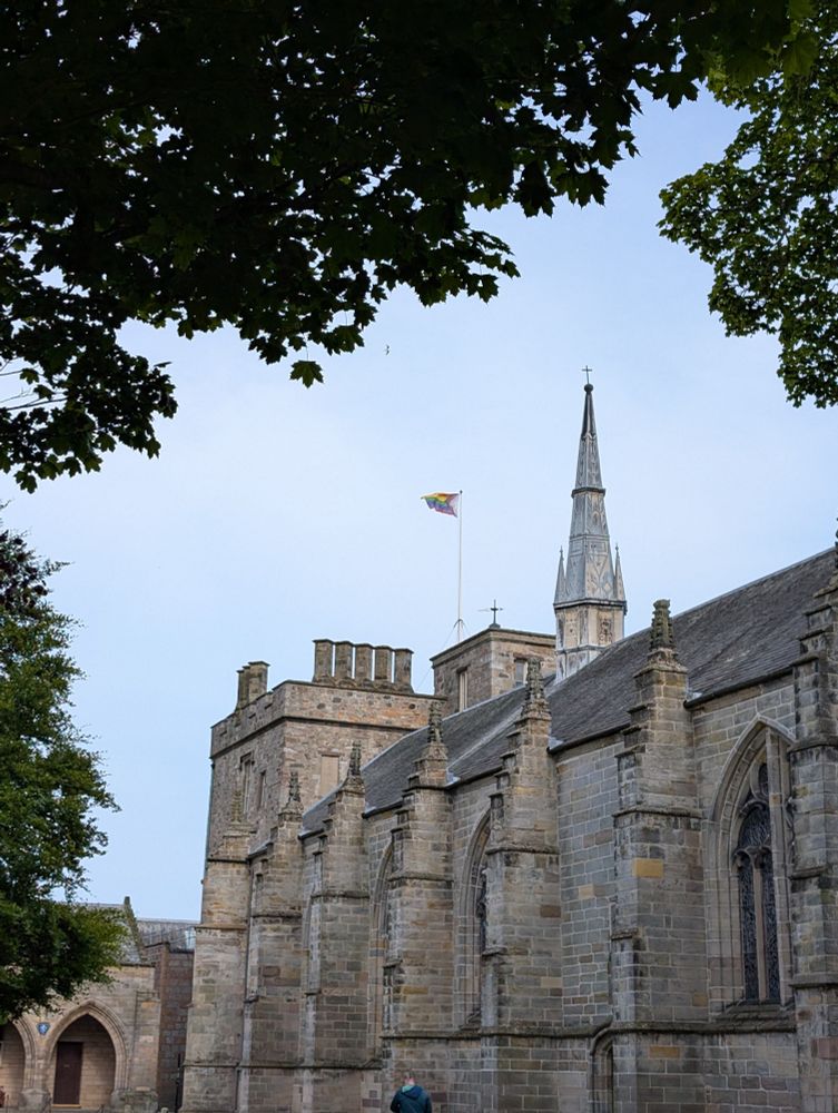 A picture of the old King's College Aberdeen university chapel building, which is in the late gothic architectural style, with with a progress pride flag flying from a flag pole atop the building.