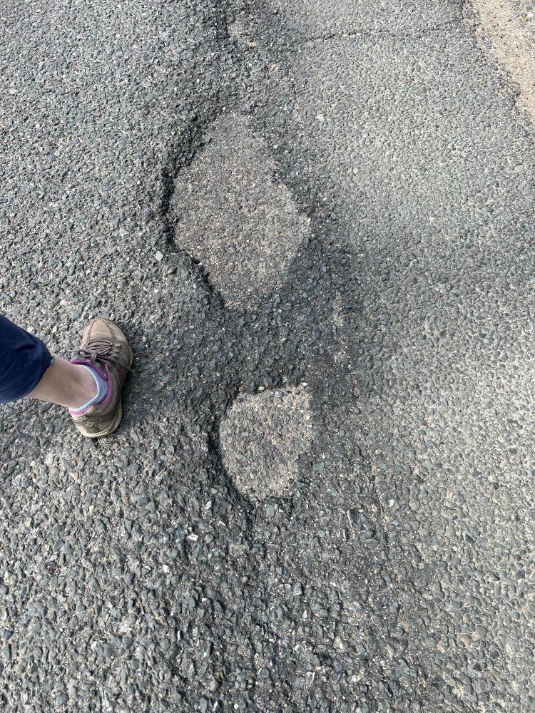 Picture of my wife’s food next to two potholes in the pavement that look like the footprint of a giant men’s dress shoe.