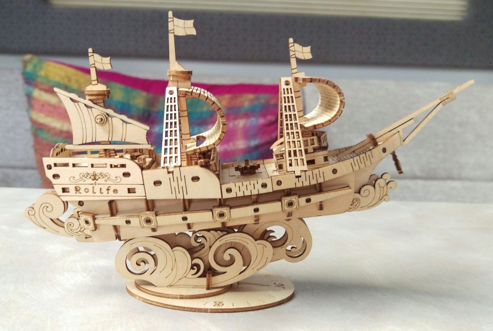 A small wooden model of a sailing ship on a base that looks like waves.