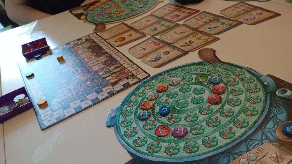 Auf einem Tisch liegt das Spiel Quacksalber, wo man Tränke braut und Zutaten auf einem Beutel zieht bis der Trank explodiert, oder man vorher aufhört, um sich mehr Punkte zu sichern. Bild aufgenommen von einem Freund, mein Arm ist auf dem Bild zu sehen.