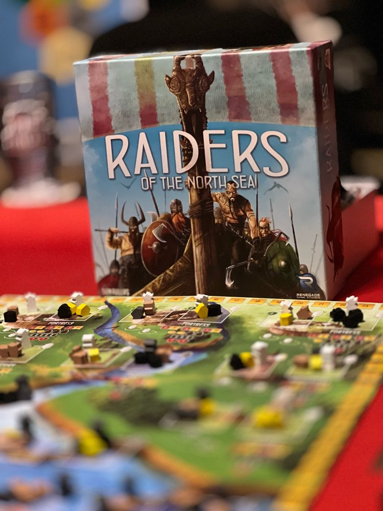 Raiders of the North Sea box top standing next to the game board, which is set up to start the game for four players.