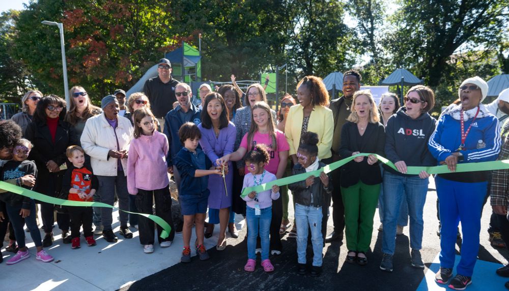 Mayor Wu cuts a green ribbon held up by community members.