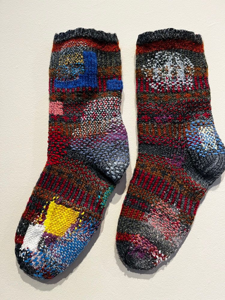 A pair of heavily-darned socks hanging on a white wall.