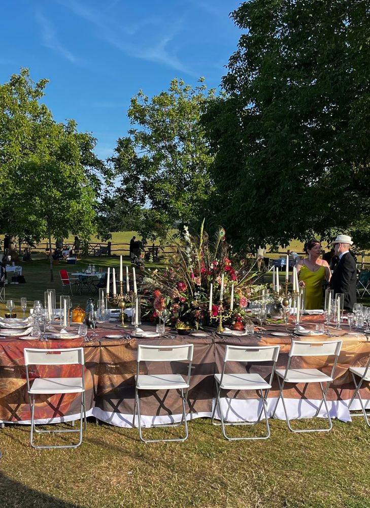 A picnic table in sunshine, fully set and with a huge floral centrepiece and candelabras.