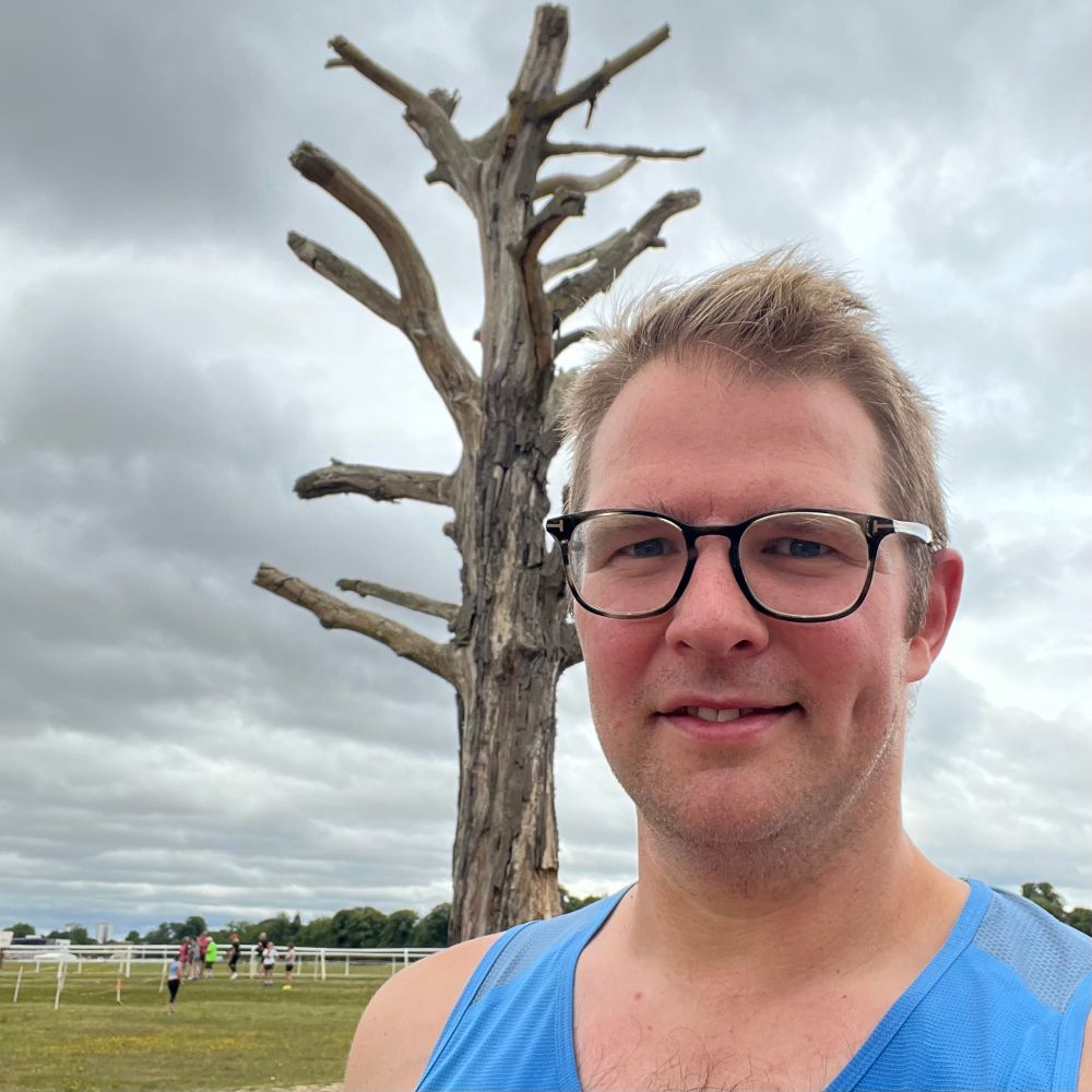 Selfie of a red-faced, sweating bespectacled man in a running vest, standing in front of the dead tree that is a landmark at Worcester Pitchcroft Parkrun