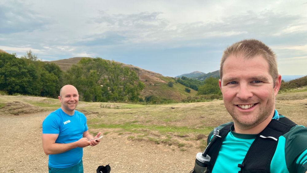 Two men in running kit on top of a hill. They are dry. They look happy.