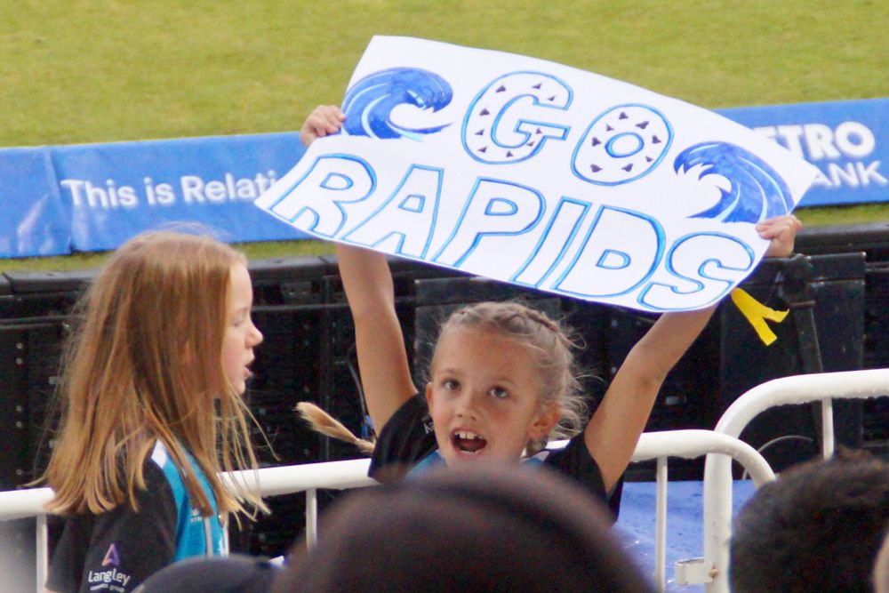 Two small girls in Worcestershire cricket shirts. One holds aloft a home-made sign reading ‘Go Rapids’.