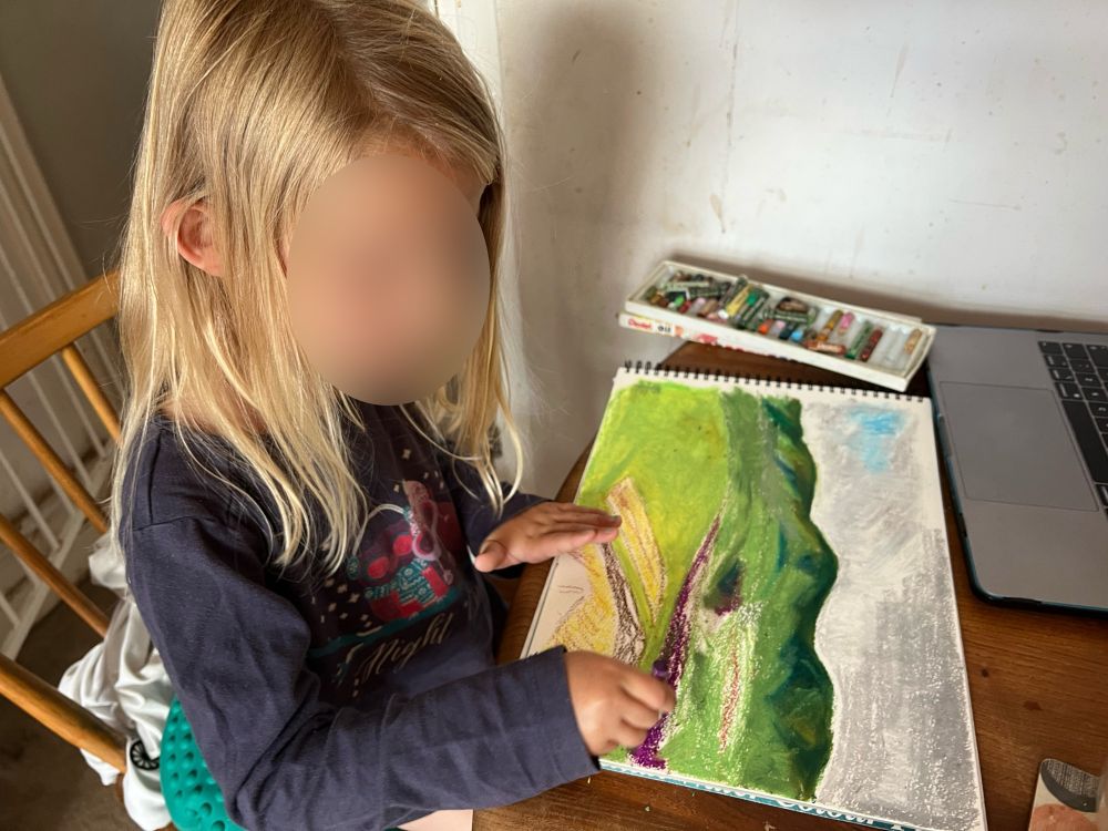 Photograph of a small child sat at a dining table, enthusiastically adding purple to the picture from the previous post.